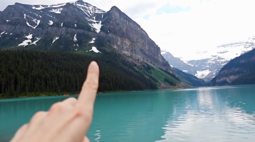 Audrey Bergner señala hacia el sendero de Fairview Lookout desde la orilla de Lake Louise en el Parque Nacional Banff, Alberta, Canadá, con el lago turquesa y picos coronados por glaciares llenando el fondo.