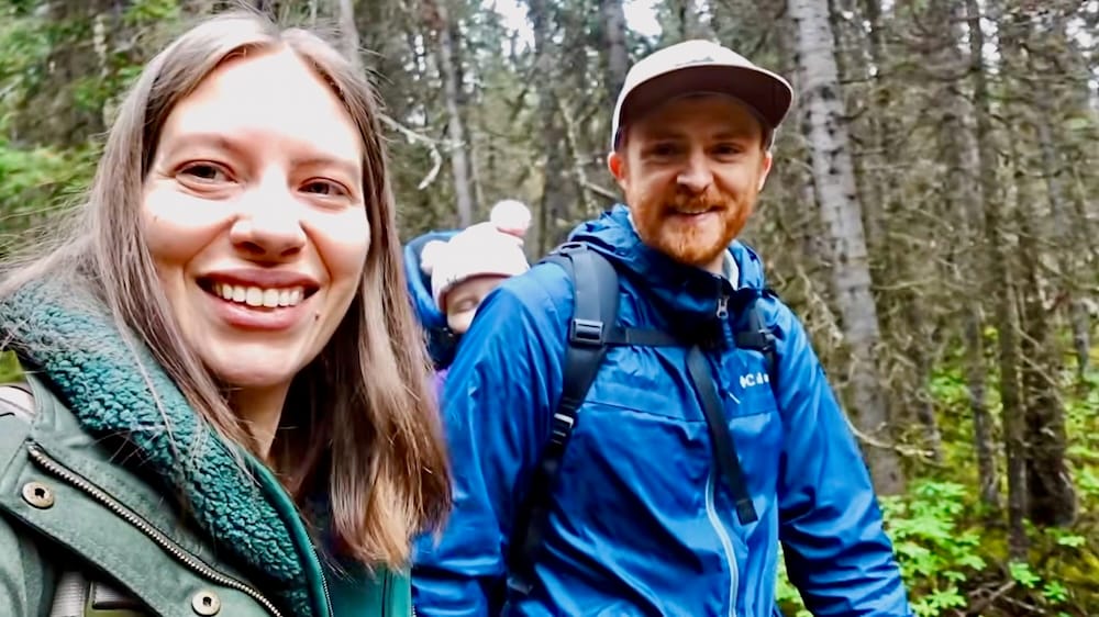 Audrey Bergner y Samuel Jeffery sonríen en el sendero boscoso de Fairview Lookout cerca de Lake Louise en el Parque Nacional Banff, Alberta, Canadá, con la bebé Aurelia Jeffery visible en una mochila portabebés detrás de ellos.