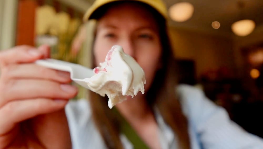 Audrey Bergner holds up a spoonful of Saskatoon Berry ice cream in close focus, with herself softly blurred in the background inside Harvey's Confectionery at Heritage Park, Calgary, Alberta, Canada.