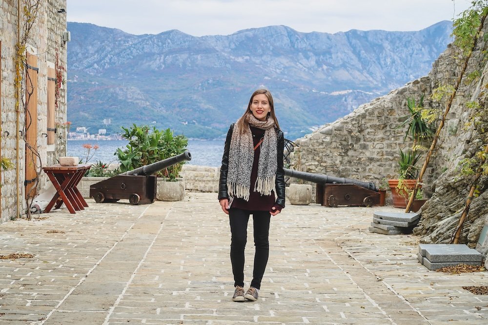 Audrey Bergner That Backpacker posing with cannons and mountain backdrop in Budva, Montenegro 