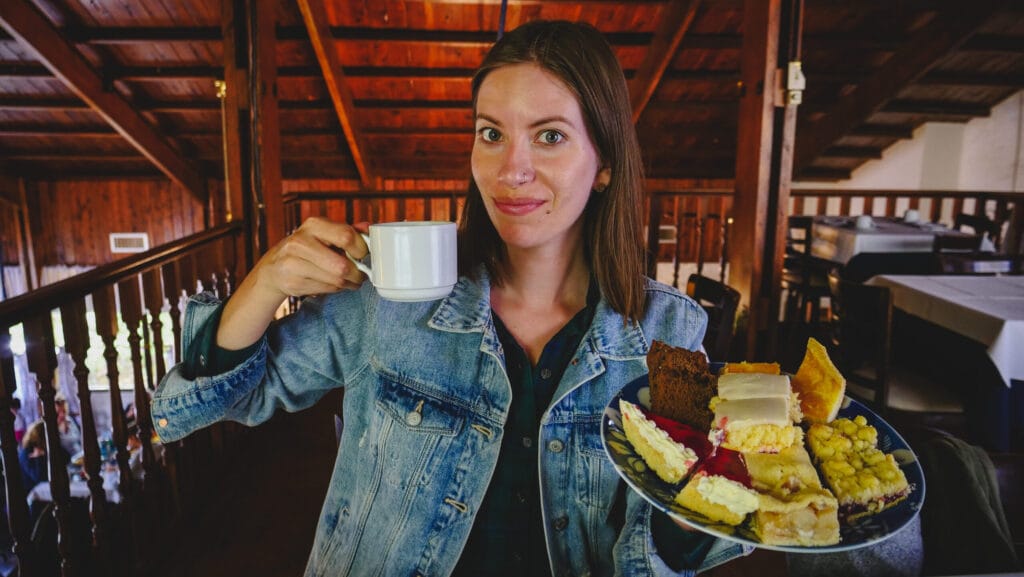 Audrey Bergner holding a plate of Welsh tea cakes and drinking tea at Ty Gwyn in Gaiman Patagonia, featuring torta negra, sponge cake, and desserts that showcase the generous portions of the traditional Welsh tea service in Argentina