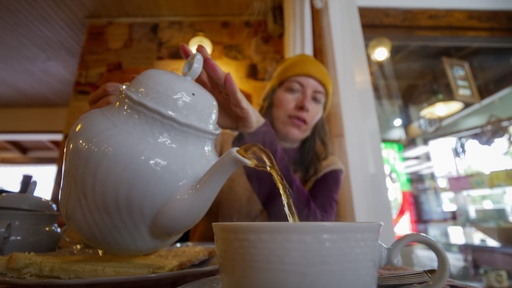 Audrey Bergner pouring tea from a teapot in Trevelin during a traditional Welsh tea service, highlighting Patagonia’s historic tea culture with pastries, cakes, and a slow, ritual-style dining experience rooted in Welsh heritage

