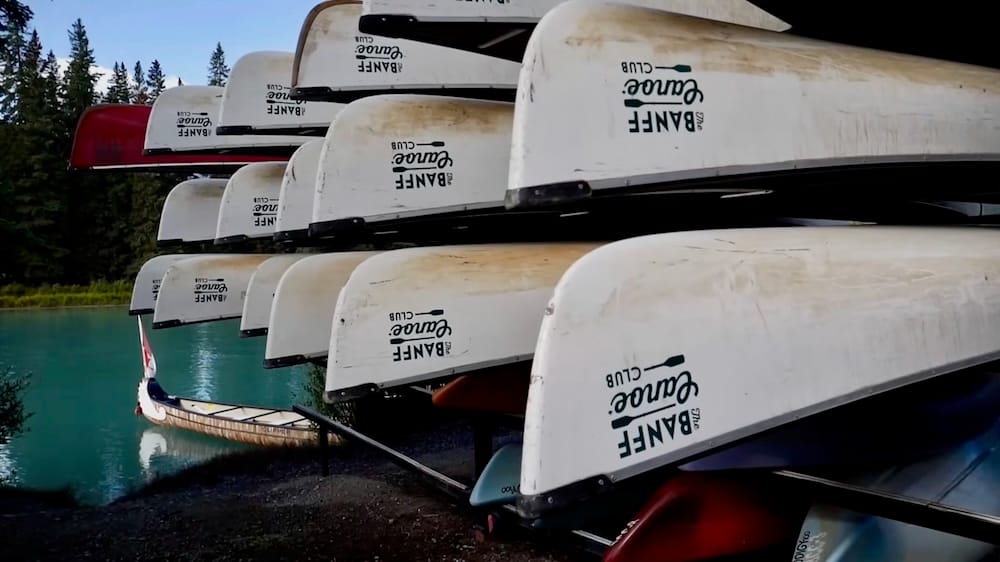 Canoas de alquiler del Banff Canoe Club junto al río Bow en Banff, Alberta, Canadá, cerca del muelle Canoas de alquiler del Banff Canoe Club apiladas junto al río Bow de aguas turquesas en Banff, Alberta, Canadá, con varios cascos blancos guardados sobre el agua cerca del muelle.