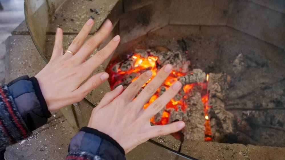 Audrey Bergner calentándose las manos junto al fuego en el Banff Cowboy Cookout, Alberta, Canadá Audrey Bergner calienta las manos sobre las brasas encendidas en el Banff Cowboy Cookout del Parque Nacional Banff, Alberta, Canadá, durante una pausa de la experiencia rústica al aire libre.