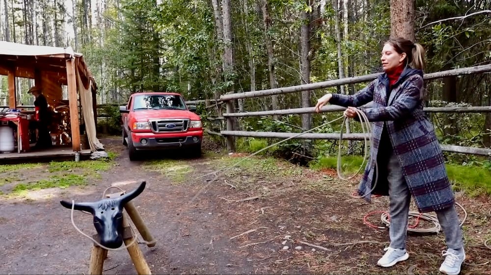 Audrey Bergner probando el lazo en el Banff Cowboy Cookout, Parque Nacional Banff, Alberta, Canadá Audrey Bergner practica con el lazo sobre un blanco con cabeza de novillo durante el Cowboy Cookout del paseo en carreta en el Parque Nacional Banff, Alberta, Canadá, junto a cercas de madera y estructuras del campamento.