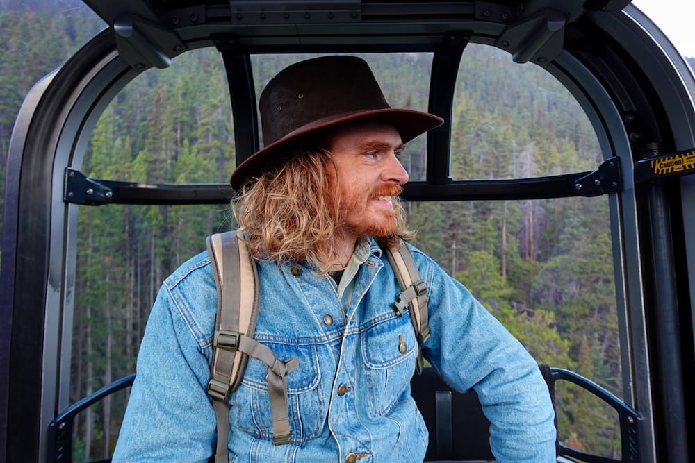 Samuel Jeffery riding the Banff Gondola on Sulphur Mountain in Banff, Alberta, Canada Samuel Jeffery rides inside the Banff Gondola on Sulphur Mountain in Alberta, Canada, looking out from the cabin with dense conifer forest and mountain slopes visible through the windows.