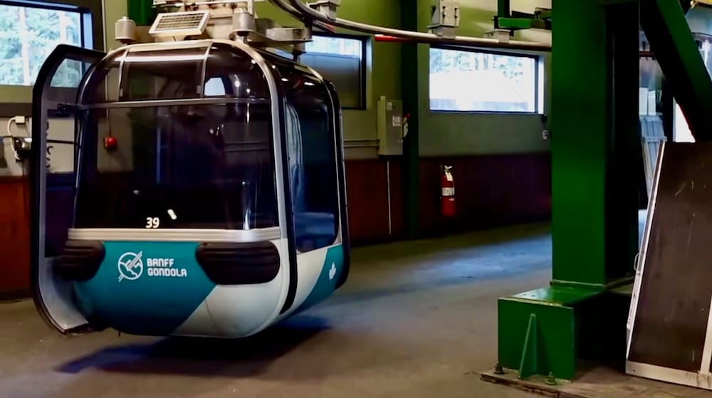 A Banff Gondola cabin inside the enclosed terminal on Sulphur Mountain in Banff, Alberta, Canada, showing the gondola car, overhead cable mechanism and indoor boarding area.