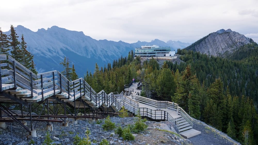 Extensa pasarela de Sulphur Mountain y edificio de la cumbre de la Banff Gondola sobre Banff, Alberta, Canadá Extenso sistema de pasarelas de madera y escaleras en la cumbre de la Banff Gondola, en Sulphur Mountain sobre Banff, Alberta, Canadá, atravesando terreno rocoso y bosque de coníferas hacia la terminal superior y las crestas montañosas.