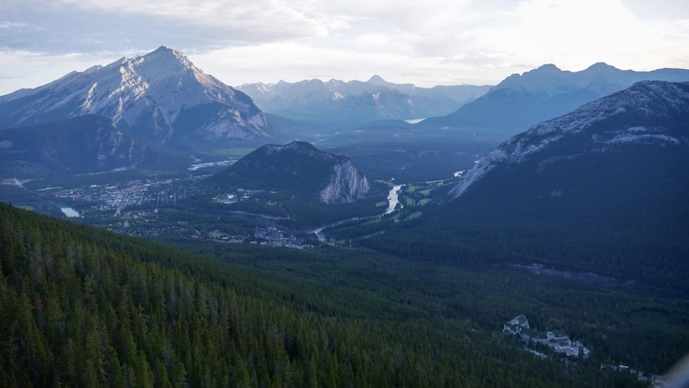 View from the Banff Gondola summit on Sulphur Mountain above Banff, Alberta, Canada, looking across Banff town, the Bow Valley, forested slopes and layered Rocky Mountain peaks in the distance.
