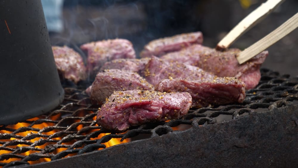 Bifes a la parrilla durante un almuerzo a caballo en el Parque Nacional Banff, Alberta, Canadá Varios bifes condimentados se cocinan sobre una parrilla al fuego durante un almuerzo de Banff Trail Riders en el Parque Nacional Banff, Alberta, Canadá, con humo elevándose alrededor de la carne.