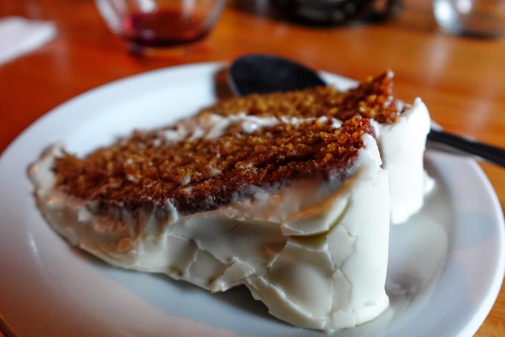 Torta de postre en un lodge durante una travesía de Banff Trail Riders en el Parque Nacional Banff, Alberta, Canadá Una porción gruesa de torta glaseada con cobertura de migas está servida en un plato blanco sobre una mesa de madera durante una travesía a caballo de Banff Trail Riders en el Parque Nacional Banff, Alberta, Canadá.