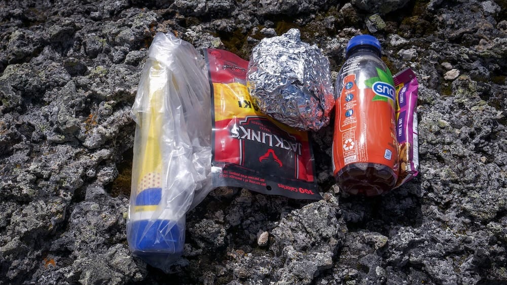 Almuerzo para llevar para el día de Allenby Pass con Banff Trail Riders en el Parque Nacional Banff Un almuerzo para llevar está apoyado sobre roca áspera durante el día de Allenby Pass con Banff Trail Riders en el Parque Nacional Banff, Alberta, Canadá, con sándwich envuelto en papel aluminio, snacks y una bebida.