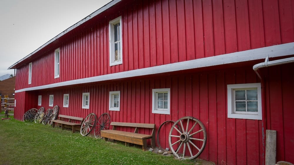 El edificio rojo de la sede de Banff Trail Riders en Banff, Alberta, Canadá, con ventanas de marco blanco, bancos de madera y viejas ruedas de carreta alineadas junto a la fachada después de la travesía.