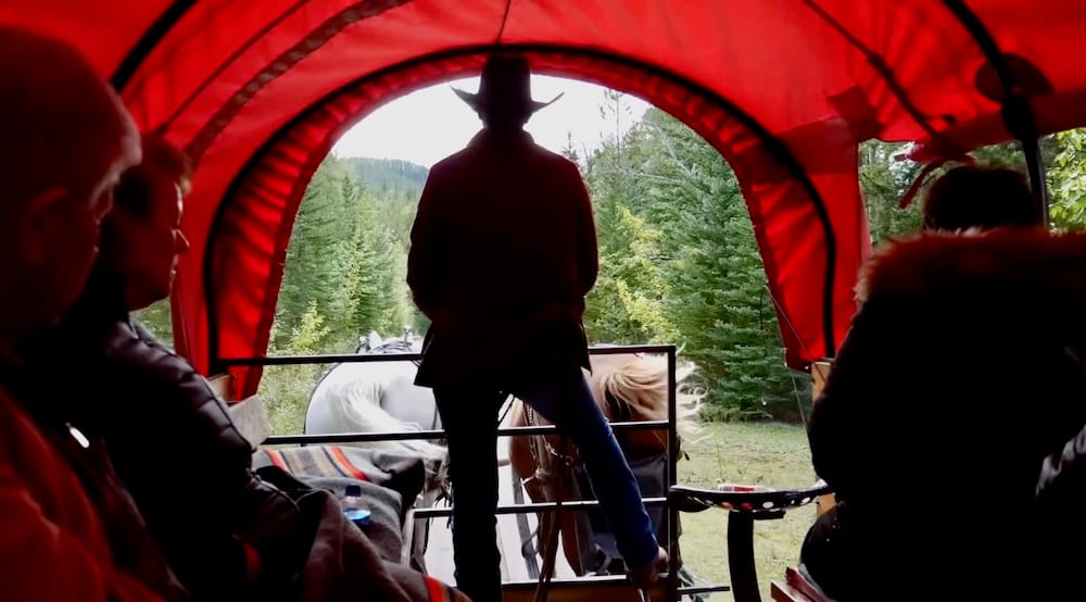 Guía del paseo en carreta de Banff con caballos en el Parque Nacional Banff, Alberta, Canadá Un guía de Banff Trail Riders va al frente de una carreta cubierta roja mientras dos caballos con arnés llevan a los pasajeros por una ruta boscosa en Banff, Alberta, Canadá.