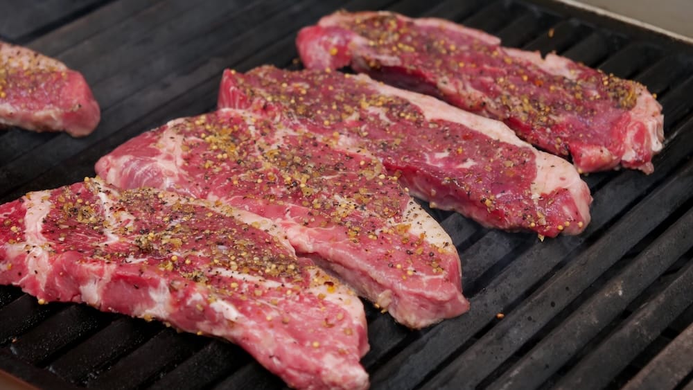 Steaks condimentados a la parrilla para el Banff Wagon Ride With Cowboy Cookout BBQ en Banff, Alberta, Canadá Varios steaks condimentados se cocinan sobre una parrilla caliente durante el Wagon Ride With Cowboy Cookout BBQ en Banff, Alberta, Canadá, como parte de la abundante comida al aire libre.