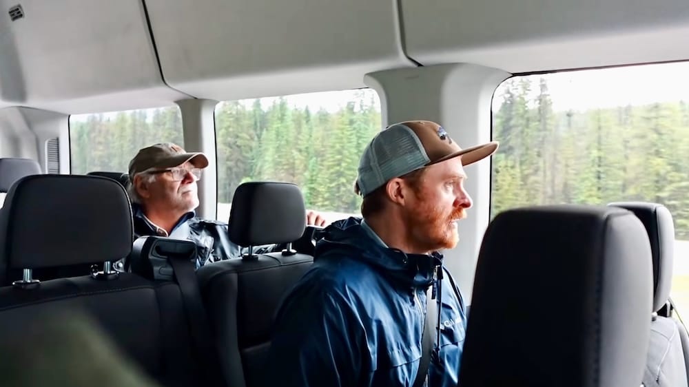 Samuel Jeffery and Daniel Bergner riding in a private Banff–Yoho tour van in the Canadian Rockies, Canada Samuel Jeffery and Daniel Bergner sit inside a passenger van during their Banff–Yoho sightseeing day in the Canadian Rockies, Canada, looking out the window as evergreen forest passes outside.