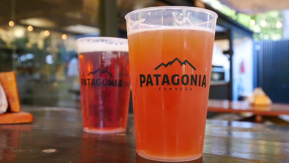 Two plastic cups of Cervecería Patagonia craft beer on a wooden table in Bariloche, Argentina, showcasing the casual brewery experience where fresh pours are enjoyed after the journey out to this iconic Lake District destination.
