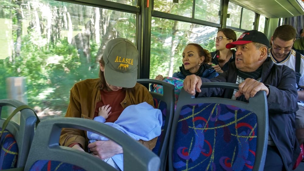 Audrey Bergner travels with Aurelia Jeffery on a public bus through the lush Andean forests near Bariloche, Río Negro, Patagonia, Argentina, while other passengers sit beside large windows.