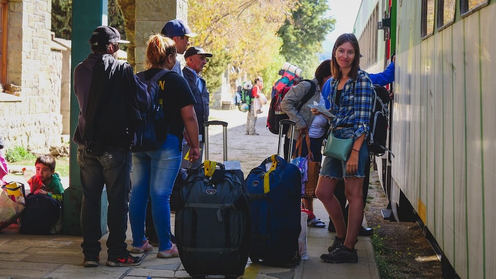 Passengers Boarding the Tren Patagónico at Bariloche Station with Audrey Bergner Audrey Bergner stands beside the Tren Patagónico as passengers board with luggage at Bariloche train station in Río Negro, Patagonia, Argentina.