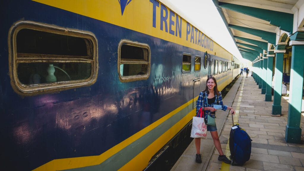 Bariloche Tren Patagónico platform scene with Audrey Bergner standing beside the blue and yellow train, documenting rail travel logistics, luggage, tickets, and overland transport in Argentine Patagonia for Project 23.