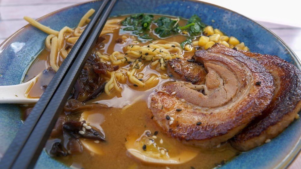 Ramen lunch at Bear Lodge Bistro, Island Lake Lodge A steaming bowl of ramen from Bear Lodge Bistro at Island Lake Lodge in Fernie, BC, topped with crispy pork belly, noodles, corn, greens, and rich broth, served as a hearty mountain-lodge lunch after a day outdoors.