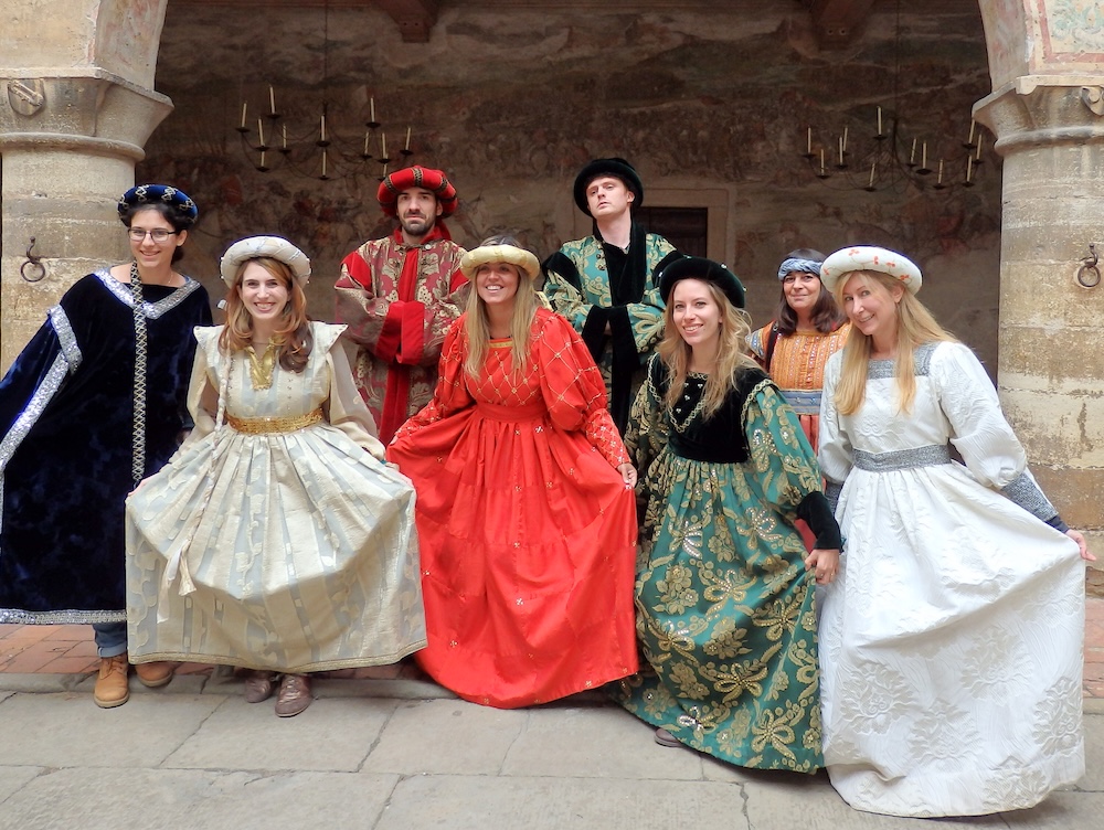 Bergamo, Italy — Audrey Bergner and Nomadic Samuel and fellow travel bloggers pose in Renaissance-style costumes during the award-winning BlogVille campaign by iAmbassador, capturing a creative storytelling moment inside a historic Italian courtyard.