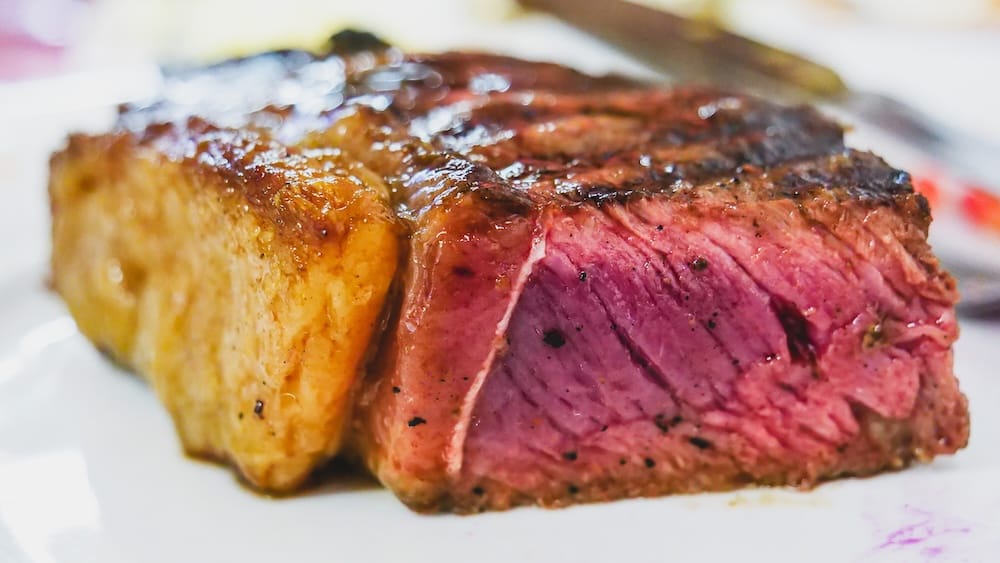 Bife de chorizo steak at De Maria Parrilla in Esquel Patagonia Argentina with juicy center and crispy fat Juicy bife de chorizo steak served at De Maria Parrilla in Esquel Patagonia Argentina, showing a perfectly cooked pink center and crispy fat layer as a classic Argentine meal during autumn travel.