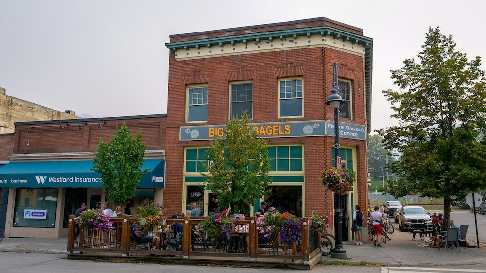 Big Bang Bagels café in downtown Fernie, British Columbia, with outdoor patio seating, hanging flower baskets, and historic brick architecture, captured as a popular food stop along the self-guided Fernie heritage walking tour.
