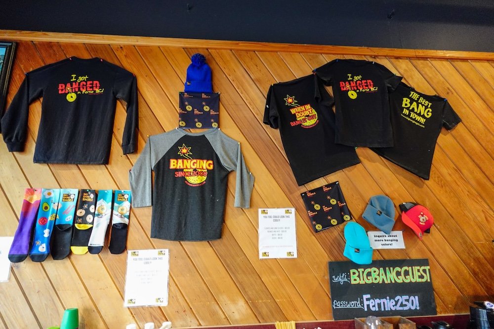 Big Bang Bagels merch wall in Fernie, BC featuring the famous “I Got Banged” slogan Big Bang Bagels merch in Fernie, British Columbia, featuring the shop’s playful “I Got Banged” shirts, hats, socks, and signage that reflect the bakery’s fun personality and cult-favorite status among locals and visitors grabbing breakfast in town.