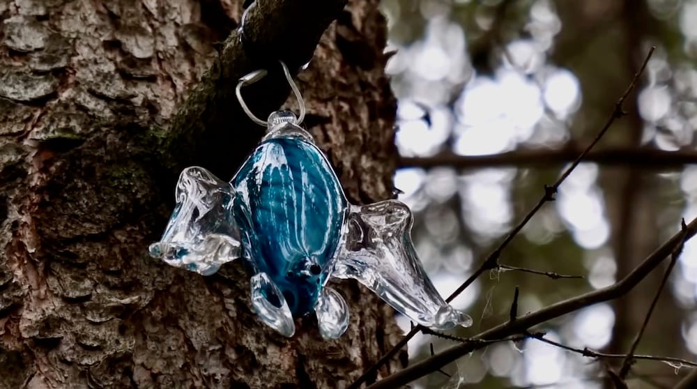 Blown-glass installation on the Art in Nature Trail, Banff, Alberta, Canada A small blue and clear blown-glass sculpture hangs from a branch against tree bark along the Art in Nature Trail in Banff, Alberta, Canada.