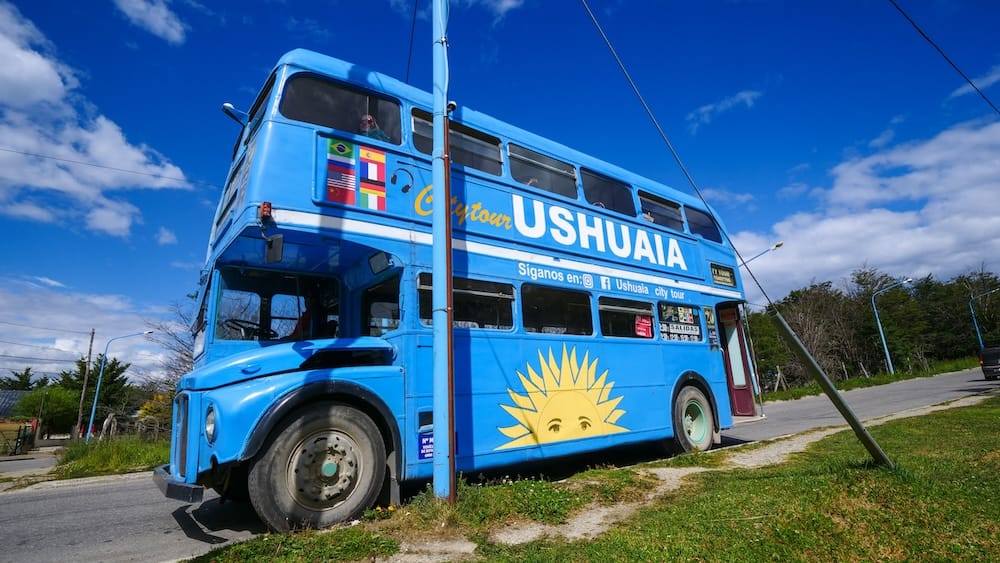 Double-decker city tour bus, Ushuaia, Tierra del Fuego, Argentine Patagonia A blue double-decker "City Tour Ushuaia" bus painted with the Sun of May, parked roadside in Ushuaia, Tierra del Fuego, Argentine Patagonia, under a clear sky.