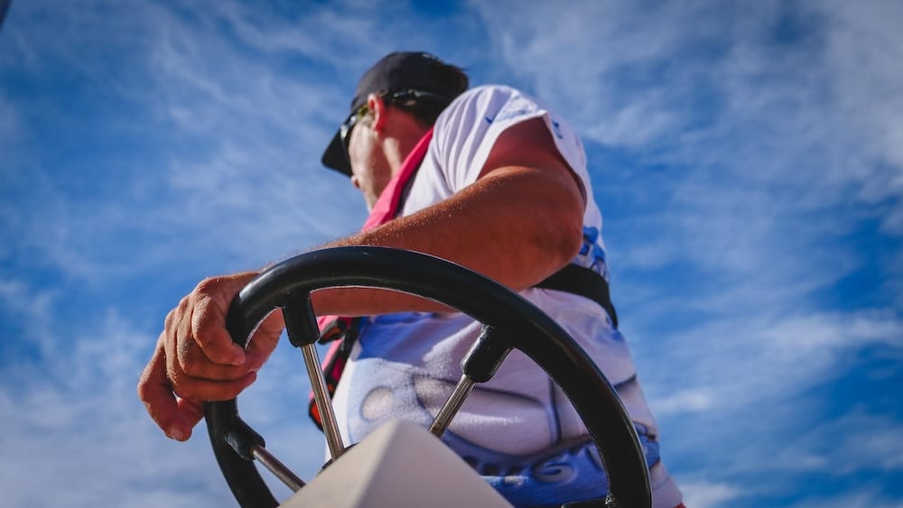 A boat captain steers a wildlife excursion in Península Valdés, Chubut, Patagonia, Argentina, seen from a low angle against a vivid blue sky, illustrating the marine access behind boat-based coastal touring.