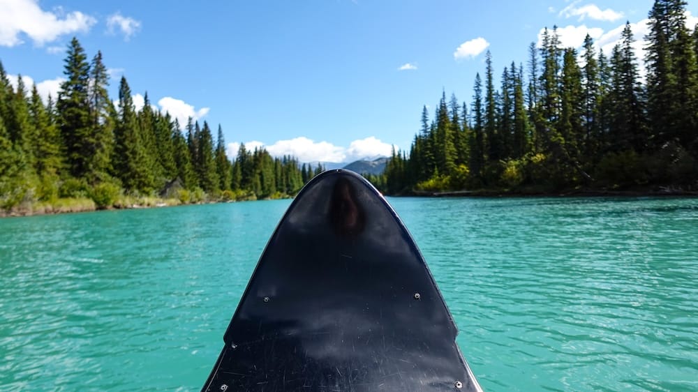 Perspectiva desde la canoa en el río Bow, Banff, Alberta, Canadá, con agua turquesa y paisaje de las Montañas Rocosas Vista a nivel de la canoa sobre las aguas turquesas del río Bow en Banff, Alberta, Canadá, con la proa en primer plano, bosque de coníferas a ambos lados y picos de las Montañas Rocosas al frente.