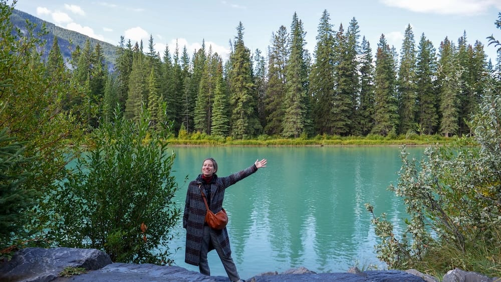 Audrey Bergner on a Bow River walk in Banff, Alberta, Canada with turquoise water and evergreen forest scenery Audrey Bergner stands beside the Bow River in Banff, Alberta, Canada, with turquoise water, dense evergreen forest and mountain slopes surrounding the riverside walking area.