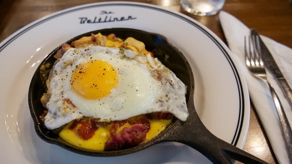 Breakfast Poutine at The Beltliner, Beltline, Calgary, Alberta, Canada A sunny-side-up egg over hash browns, bacon, and cheese in a cast-iron skillet, served on a plate branded "The Beltliner," at the restaurant in Beltline, Calgary, Alberta, Canada.
