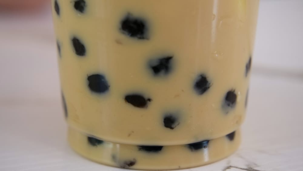 Close-up of a bubble tea drink in Calgary Chinatown, Alberta, Canada, showing creamy milk tea filled with dark tapioca pearls in a clear plastic cup.