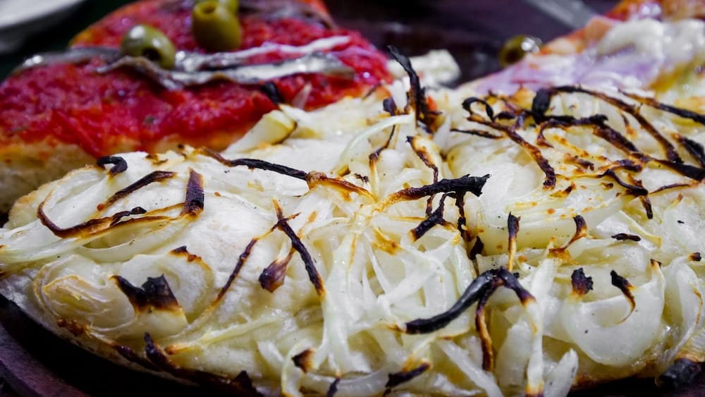 Buenos Aires Argentina thick crust pizza at El Cuartito topped with melted mozzarella onions and anchovies showing classic al molde style with dense dough and heavy cheese typical of traditional Buenos Aires pizza culture