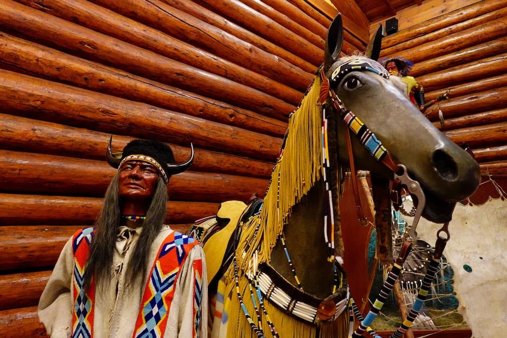 Cultural display inside Buffalo Nations Museum in Banff, Alberta, Canada, featuring a decorated horse, life-size figures, beadwork and traditional clothing against rustic log walls.