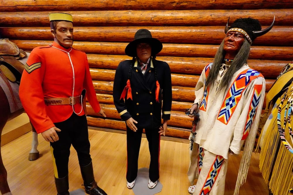 Diorama cultural con Policía Montada y figuras indígenas en Buffalo Nations Museum, Banff, Alberta, Canadá Exhibición interior de Buffalo Nations Museum en Banff, Alberta, Canadá, con una figura de la Policía Montada junto a figuras indígenas con ropa detallada frente a una pared de troncos.