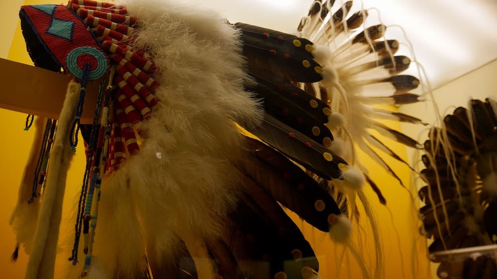 Detalle de tocado de plumas y trabajos de cuentas en Buffalo Nations Museum, Banff, Alberta, Canadá Primer plano de un tocado de plumas con trabajos de cuentas de colores y detalles decorativos dentro de Buffalo Nations Museum en Banff, Alberta, Canadá, con más piezas de plumas detrás.