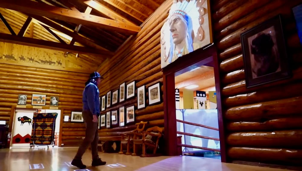 Samuel Jeffery en la exhibición interactiva de lenguas de las Primeras Naciones en Buffalo Nations Museum, Banff Samuel Jeffery usando la exhibición interactiva sobre lenguas de las Primeras Naciones dentro de Buffalo Nations Museum en Banff, Alberta, Canadá, rodeado de cuadros y paredes de troncos.