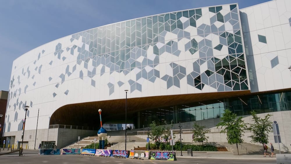Calgary Central Library Exterior in East Village Alberta Canada with Geometric Modern Architecture Exterior of Calgary Central Library in East Village, Calgary, Alberta, Canada, showing its sweeping white facade, geometric window pattern, broad entrance and colourful street-level barriers.