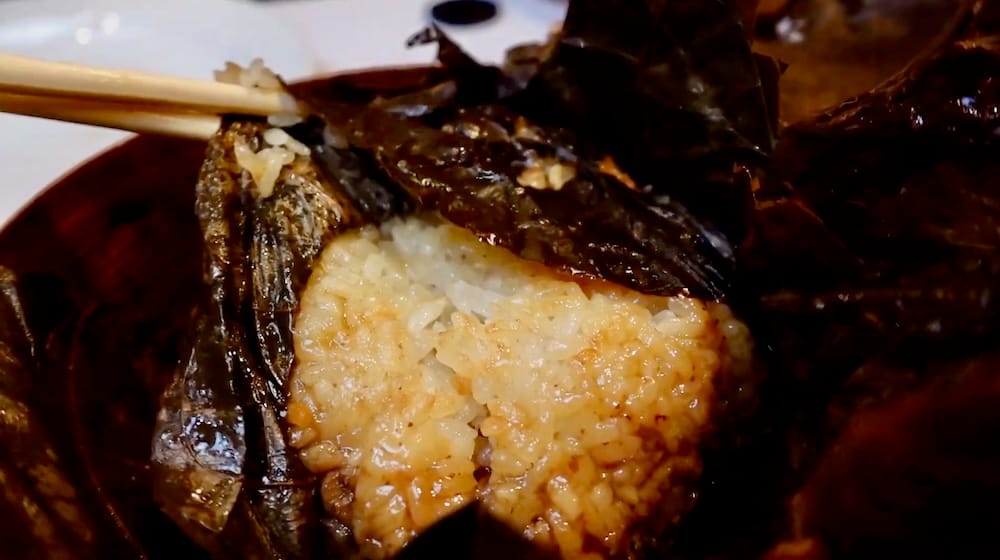 Close-up of sticky rice wrapped in lotus leaf in Calgary Chinatown, Alberta, Canada, with chopsticks lifting a section to show the glossy rice and dark leaf from a dim sum meal.
