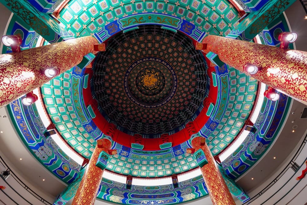 Cúpula circular ornamentada dentro del Calgary Chinese Cultural Centre, en Calgary, Alberta, Canadá, con detalles pintados en turquesa, azul, rojo y dorado enmarcados por altas columnas rojas.