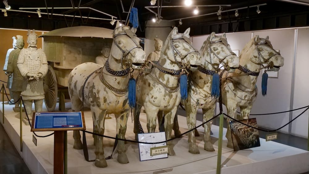 Réplicas de guerreros de terracota, caballos y un carro exhibidas dentro del Calgary Chinese Cultural Centre Museum en Calgary, Alberta, Canadá, con paneles interpretativos alrededor de la muestra.