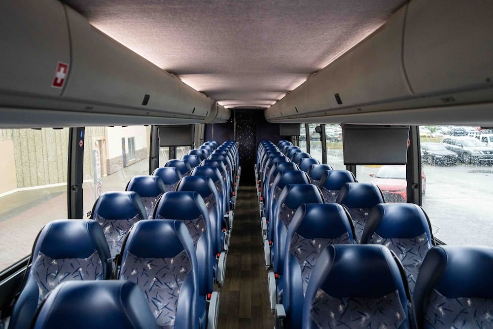 Interior de un micro interurbano utilizado en la ruta Calgary-Edmonton, Alberta, Canadá, con filas de asientos azules, compartimentos superiores para equipaje y un pasillo central.