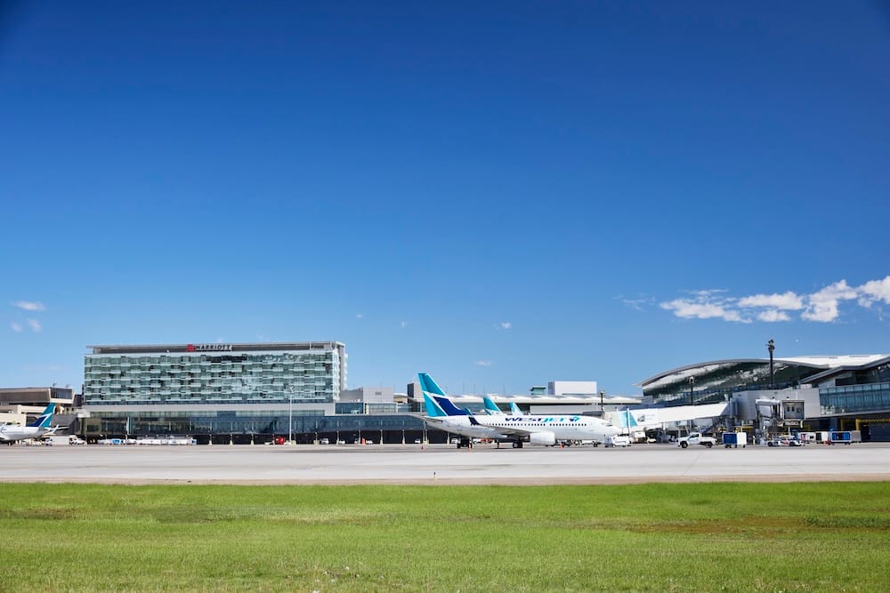 Calgary International Airport in Alberta, Canada, with WestJet aircraft parked beside the terminal and airport hotel under a clear blue sky, illustrating the city’s role as an Alberta air gateway.