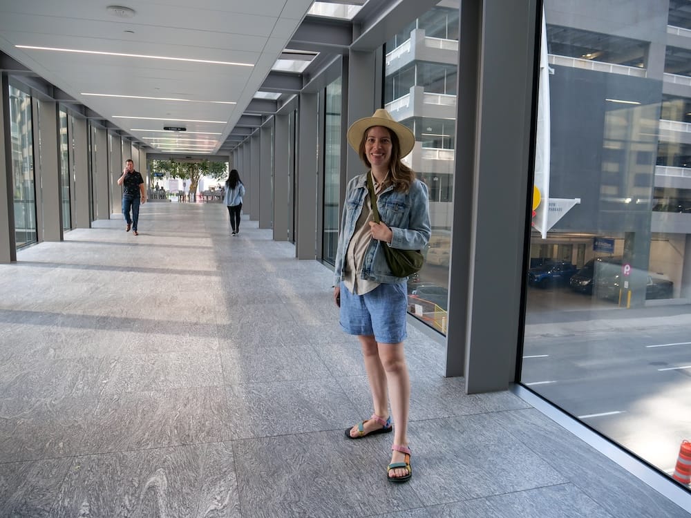 Calgary Plus 15 Network Downtown Alberta Canada with Audrey Bergner Inside the Enclosed Skywalk Audrey Bergner stands inside Calgary’s +15 Network in downtown Calgary, Alberta, Canada, surrounded by glass walls, enclosed pedestrian walkways and views of nearby office buildings.