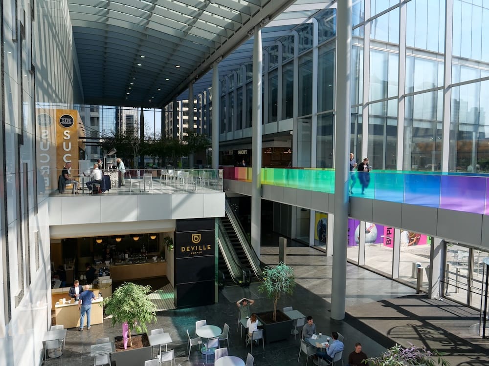 Vista interior amplia del Calgary +15 Skywalk en el centro de Calgary, Alberta, Canadá, con un corredor elevado vidriado sobre cafés, zonas para sentarse, escaleras mecánicas y espacio público interior.