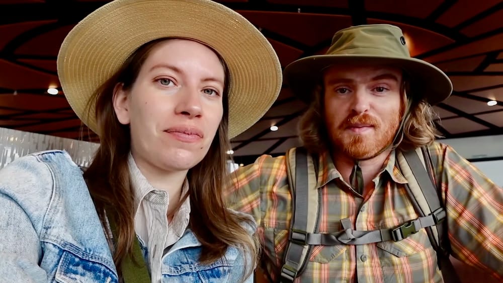 Samuel Jeffery y Audrey Bergner juntos dentro de la red Calgary +15 Skywalk en el centro de Calgary, Alberta, Canadá, con sombreros de verano y ropa informal de paseo durante su visita a la ciudad.